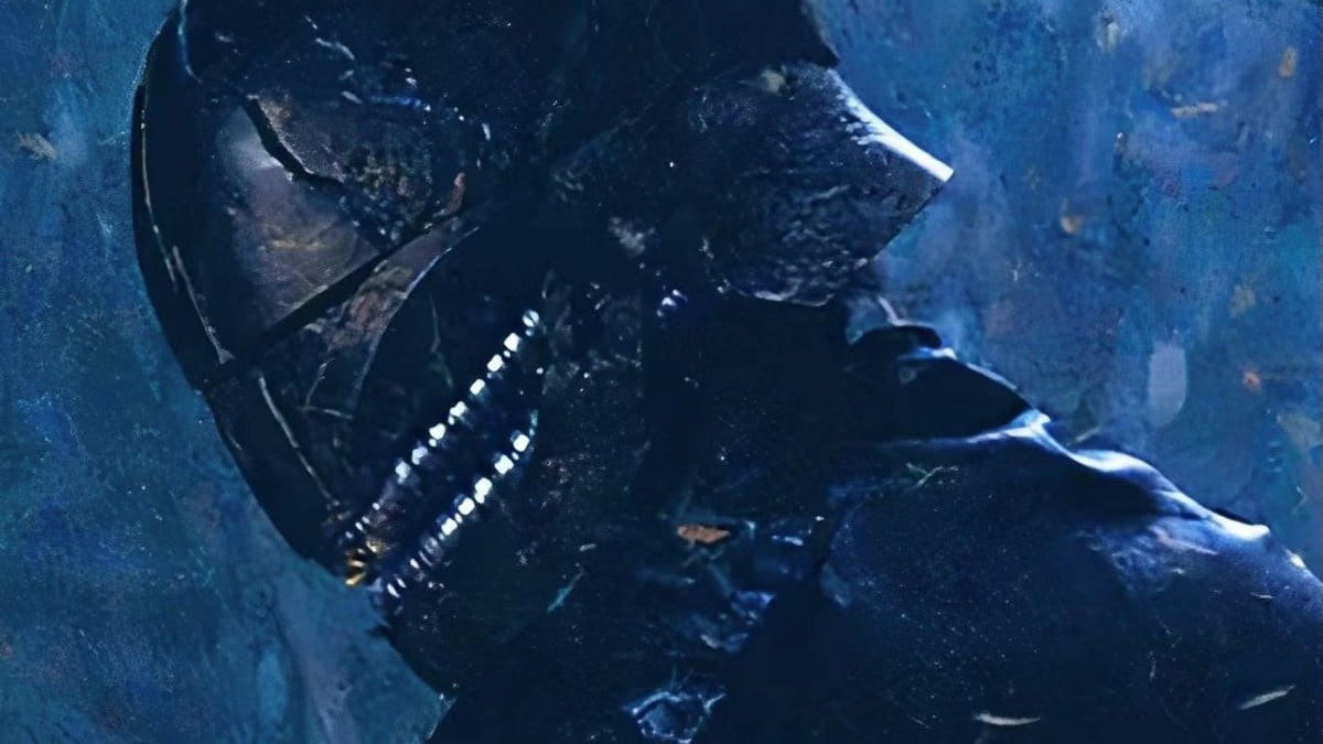 Manny Jacinto as Qimir in the Disney+ Star Wars show, 'The Acolyte.' It's a close-up of Qimir turned to the side in a black helmet that covers his whole face. It has silver detailing around the mouth area that make it look like the helmet has a big creepy smile. He's dressed all in black.