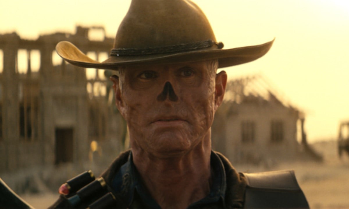 Walton Goggins as The Ghoul in Prime Video's 'Fallout.' He is a man who has been irradiated to the point of his skin being red and wrinkly, having no hair, and no nose. He's wearing a cowboy hat and strapped with weapons as he walks through the Wasteland.